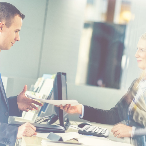 Photo of a woman handing a sheet of paper to a man in an office 